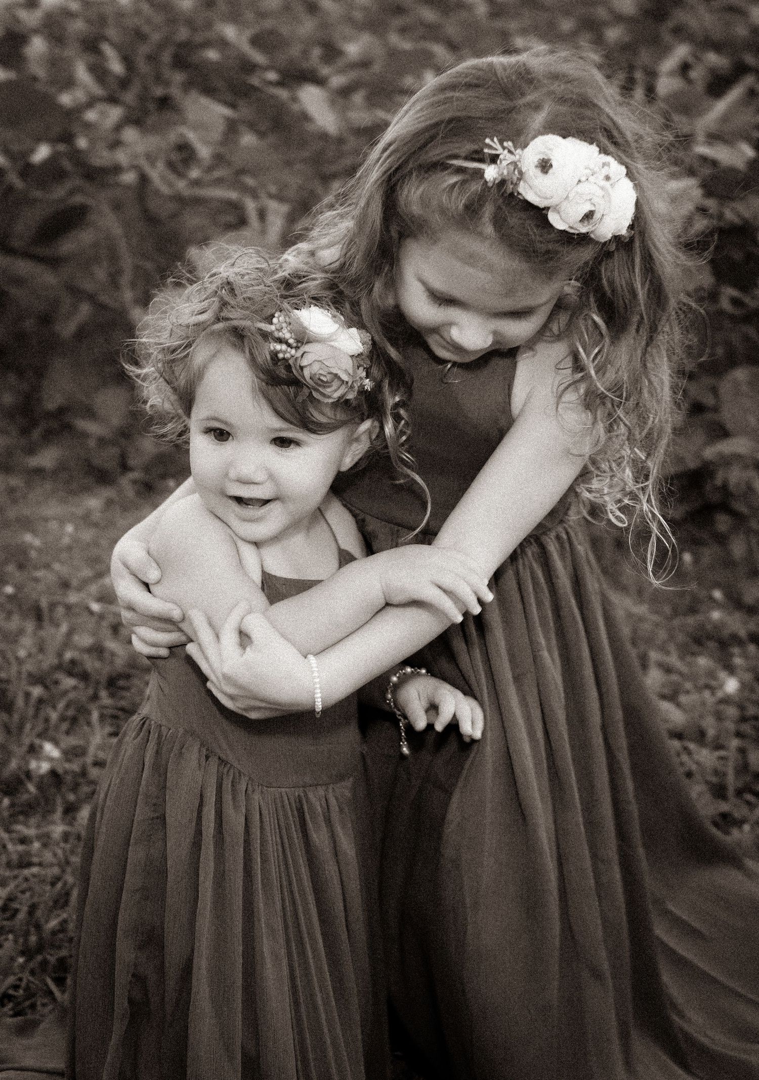 Two girls in matching dresses sharing sweet moment in black and white photograph.