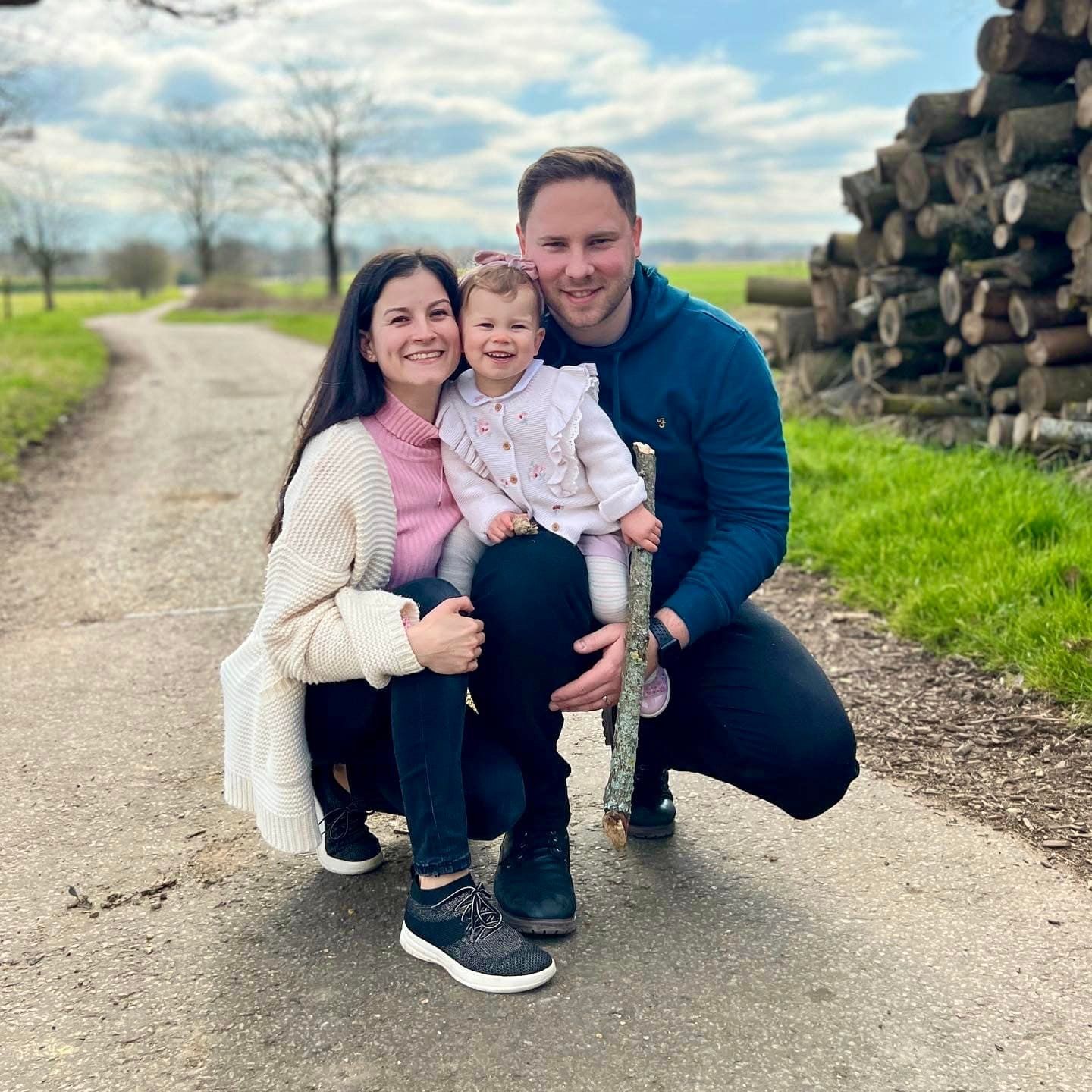 Family portrait on country path with woodpile in background on sunny spring day.