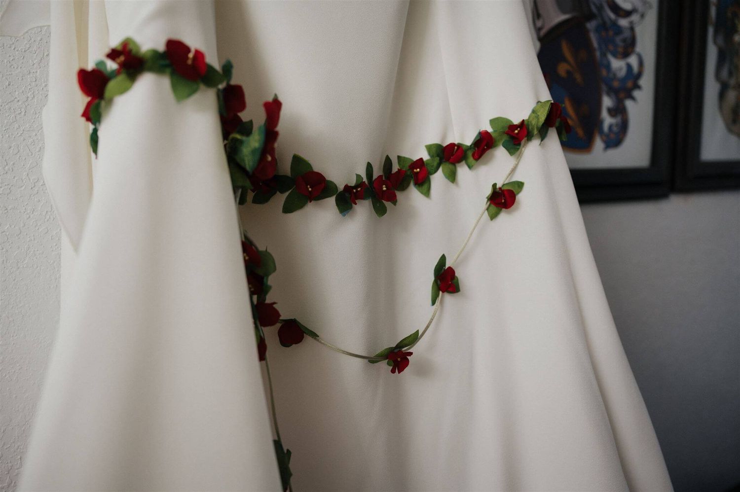 Close-up of a white wedding dress adorned with delicate red rose garlands.
