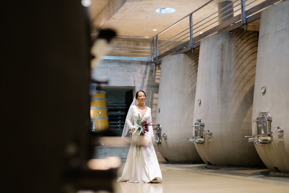 Elegant bridal portrait in flowing white dress among industrial wine tanks.
