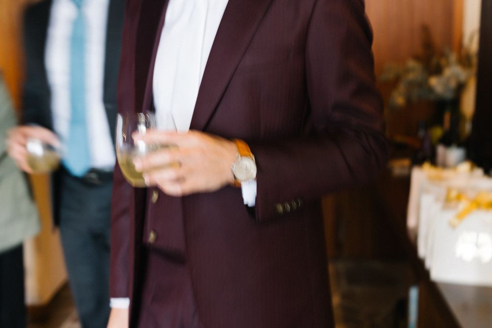 Elegant burgundy three-piece suit with white shirt and brass buttons hanging on display.