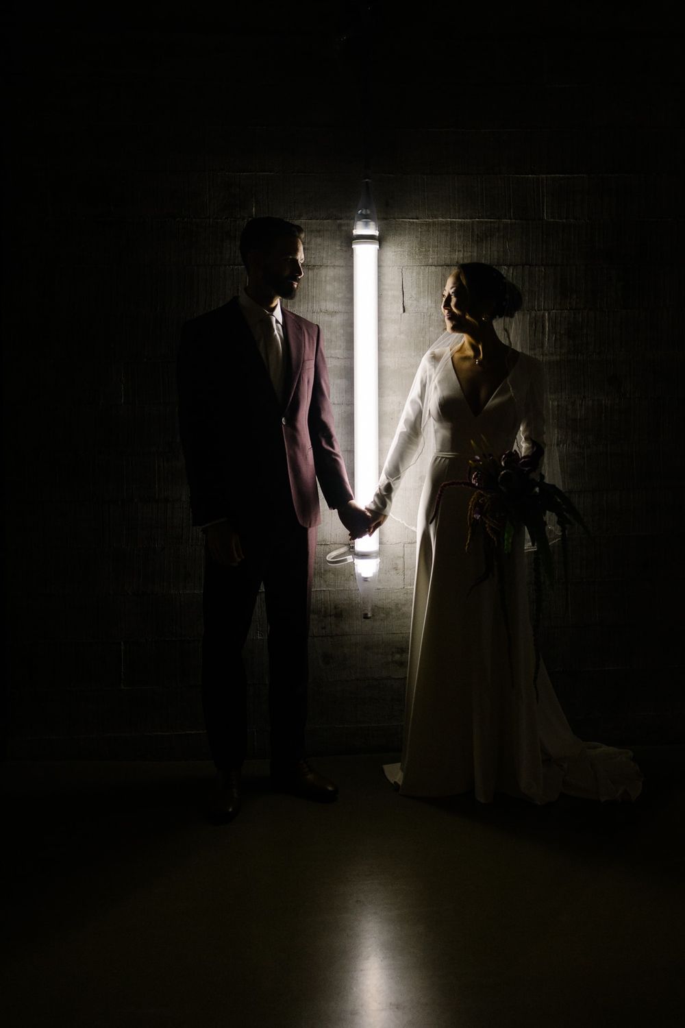 Dramatic silhouette of couple holding hands in dark hallway with single light source.