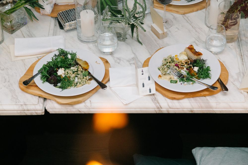 Two elegant place settings with fresh salads on marble plates against a white tablecloth.