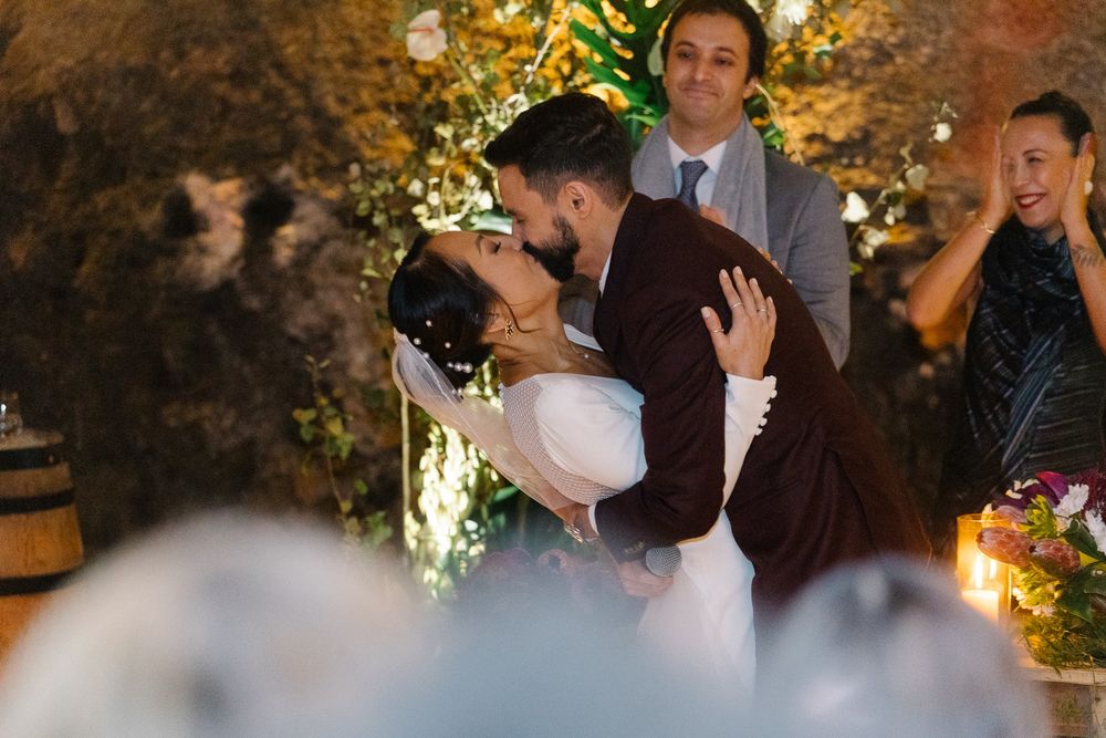 Wedding ceremony kiss with officiant and guests in romantic lit setting.