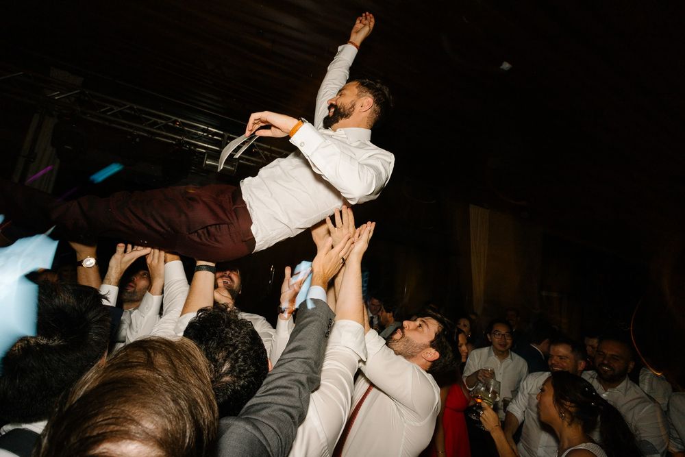 A person crowd surfing at a lively party or concert with outstretched arms being supported by the crowd below.