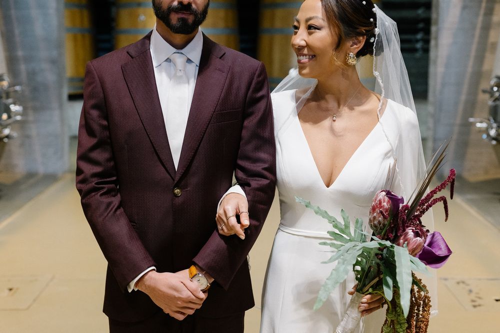 Wedding couple in burgundy suit and elegant white dress holding a purple bouquet.