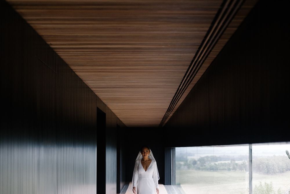 A silhouette of a bride in white against a dark modern hallway.
