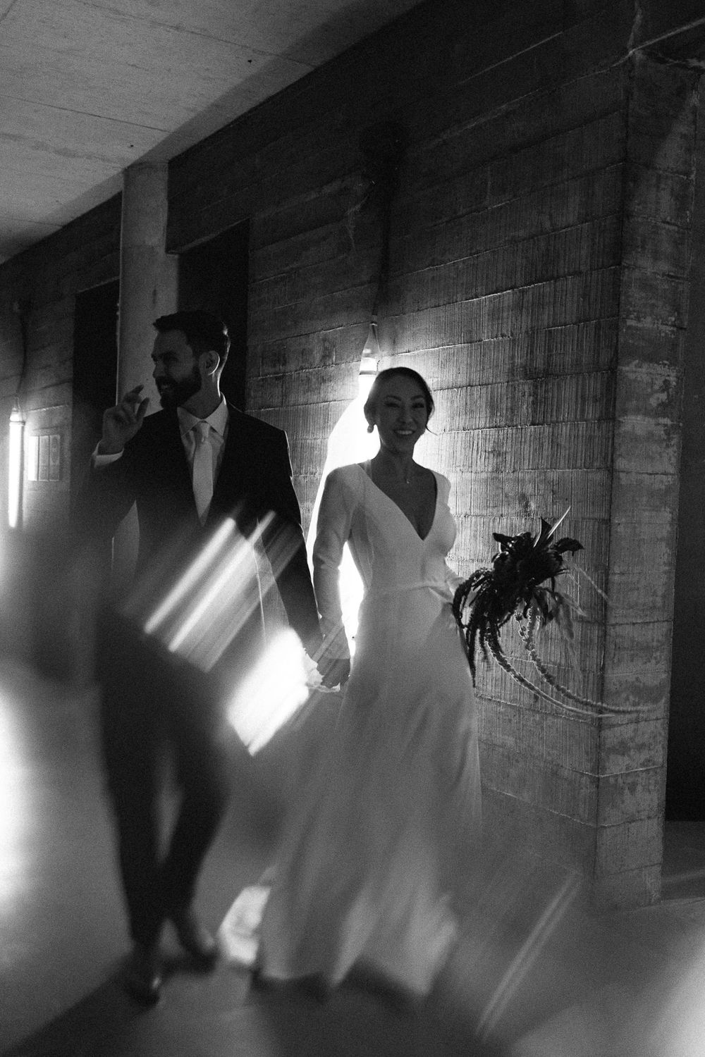 Wedding couple walking through an industrial space with sunlight streaming through windows.