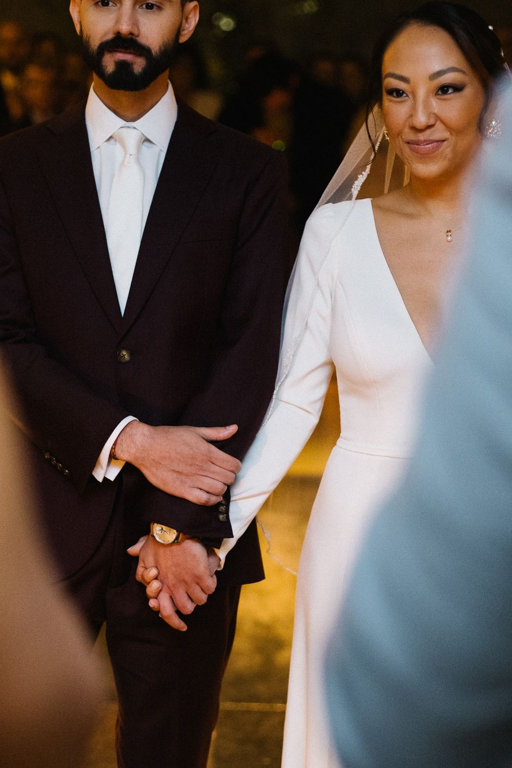 Close-up of newlyweds holding hands in formal attire.