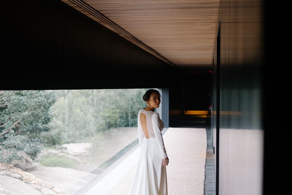 A bride in a minimalist white wedding gown stands on a modern balcony.