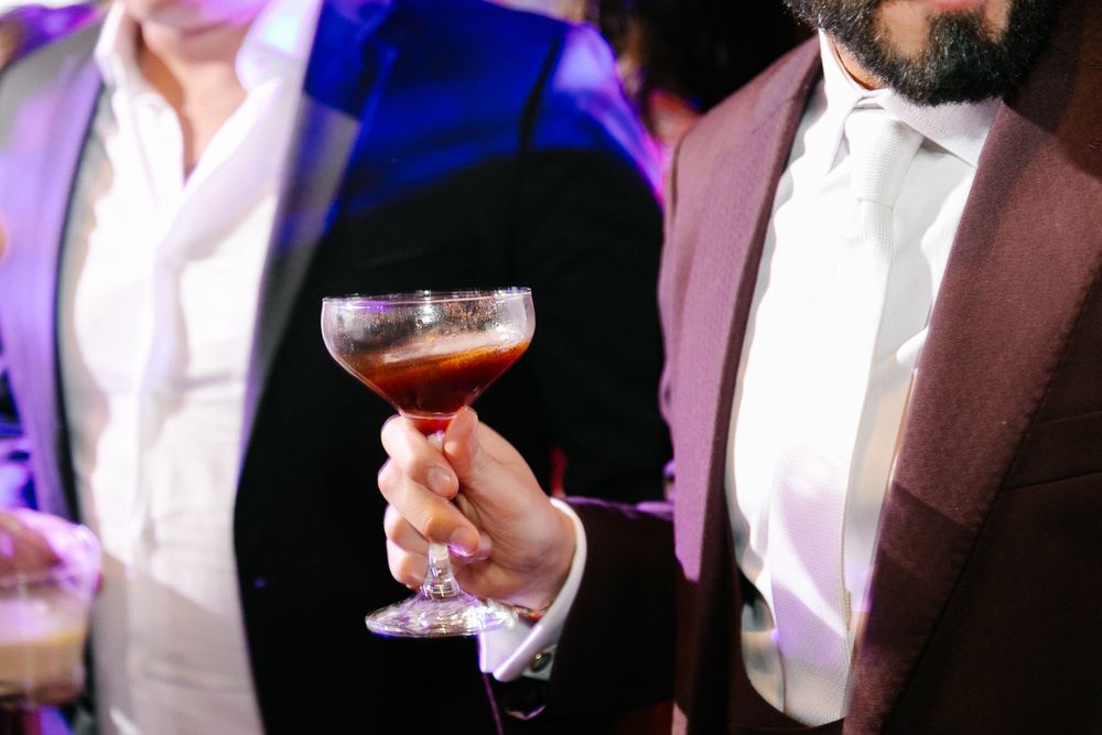 Close-up of a hand holding a cocktail glass with formal attire in purple lighting.