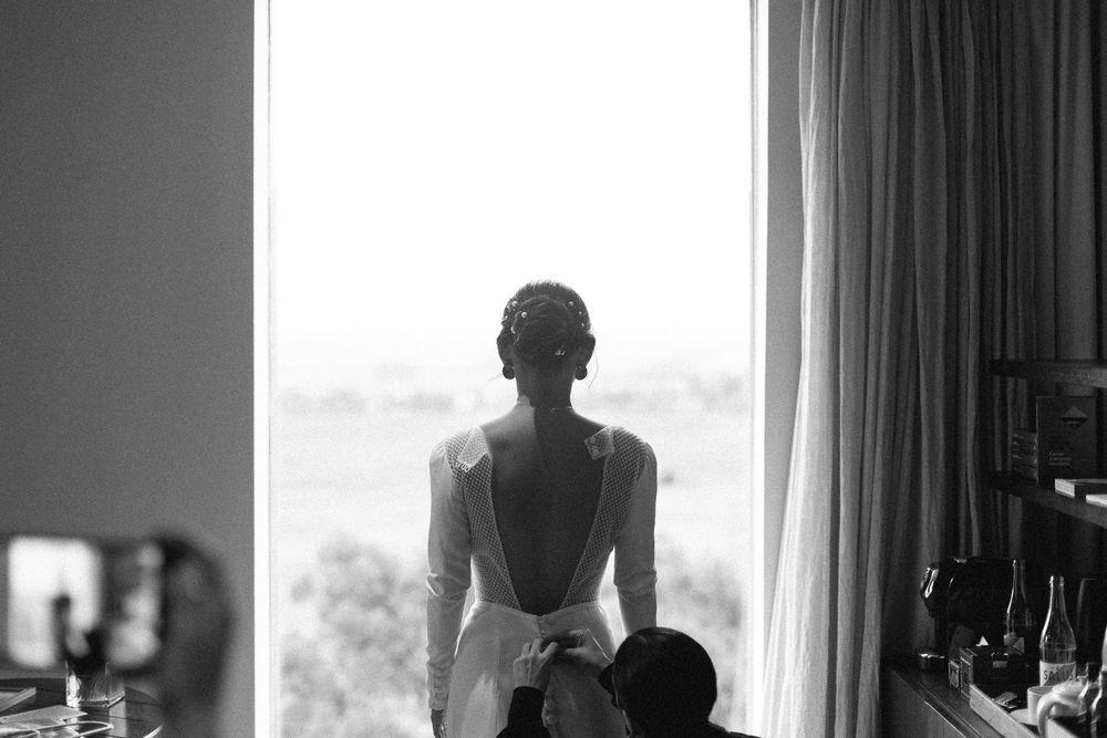 A black and white image of someone in a wedding dress looking out a window.