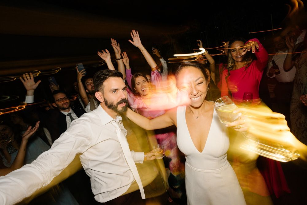 Dynamic shot of wedding guests dancing with motion blur and festive lighting.