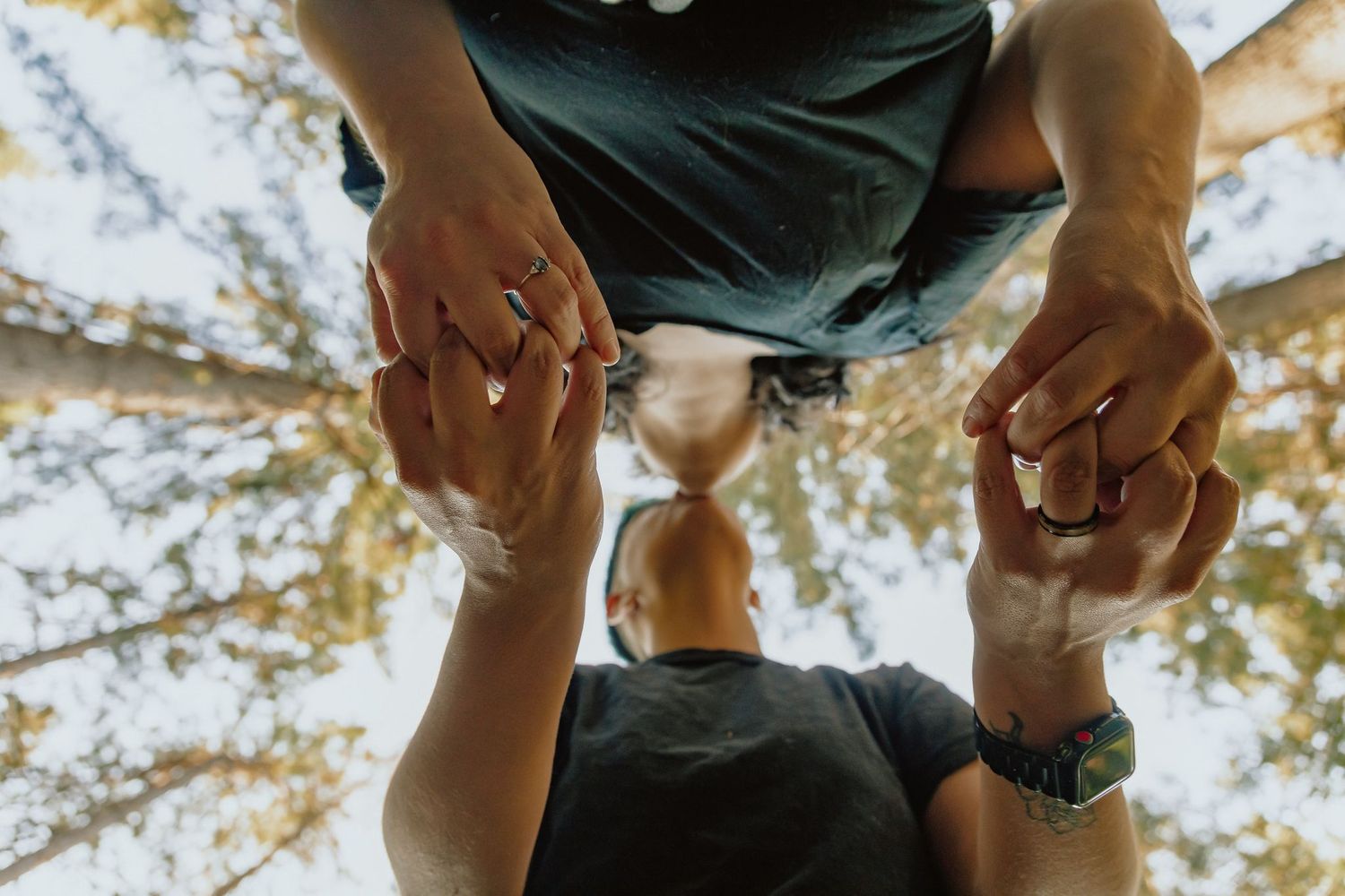 Low angle view of hands lifting someone in the air with trees in background.
