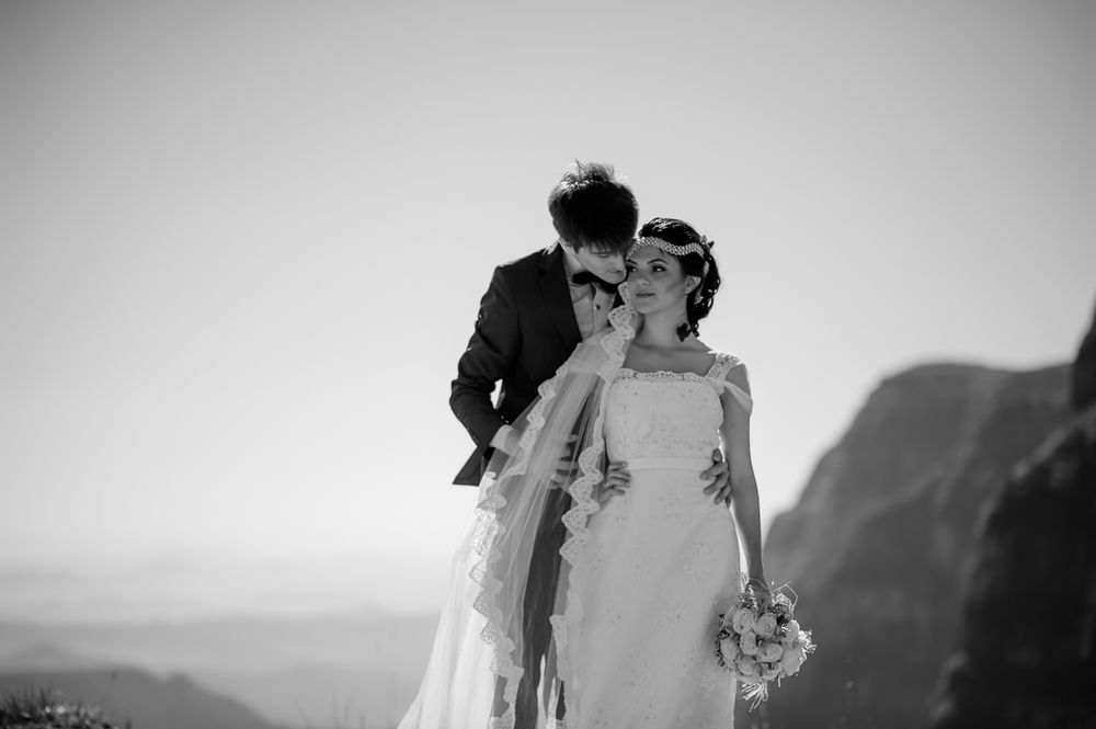 Black and white portrait of couple in wedding attire with mountainous backdrop.