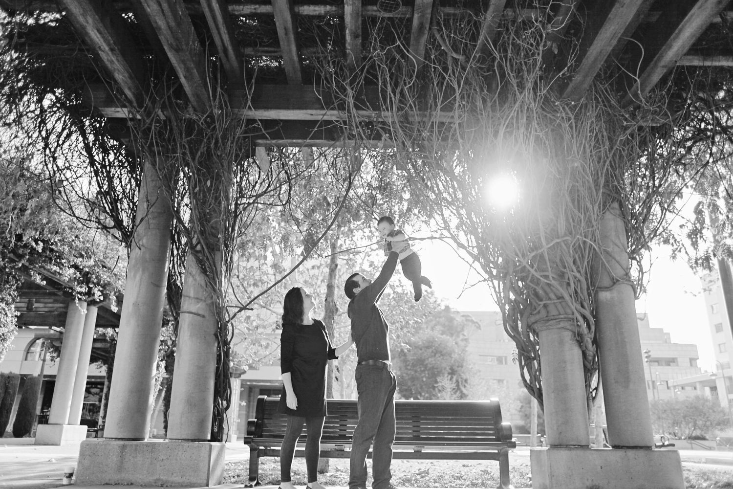 Silhouette of family lifting child together under covered walkway at sunset.