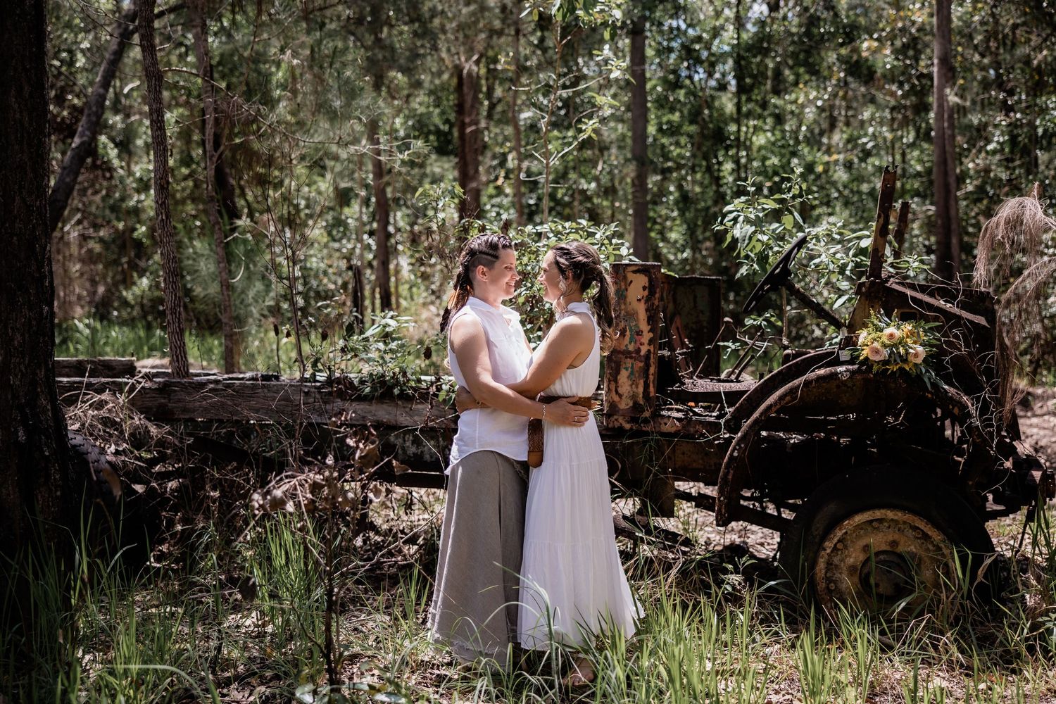 Two people embracing in a sunlit forest with rustic wooden logs in the background.