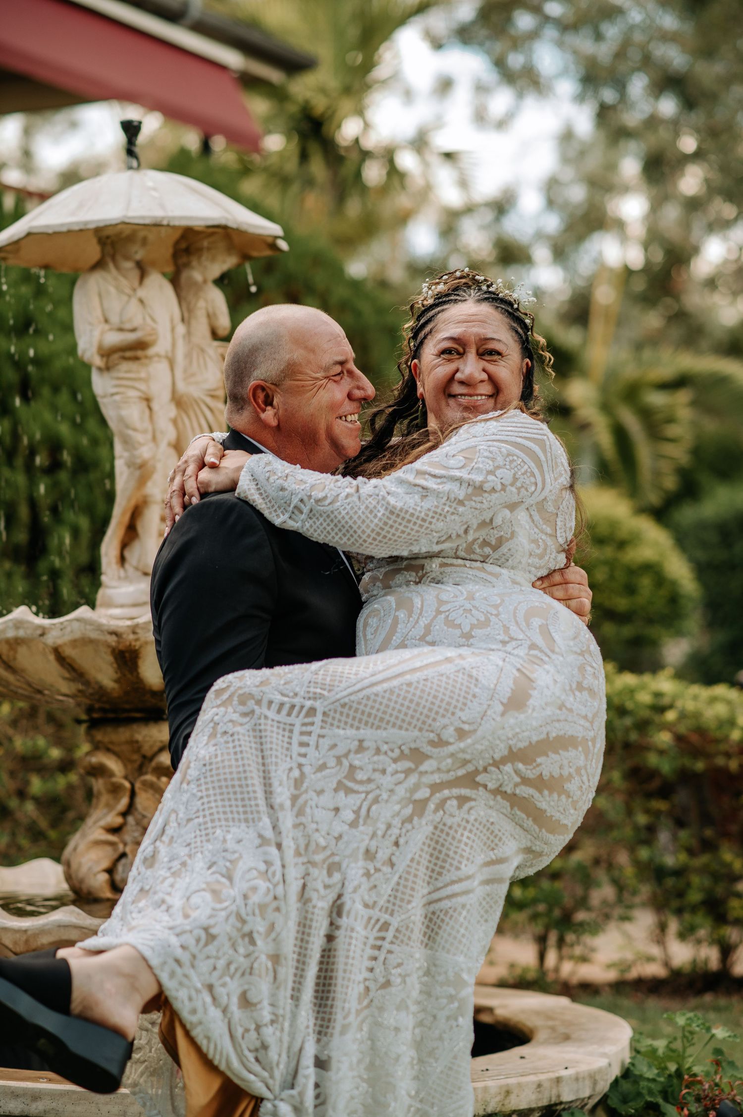 Joyful wedding moment captured by garden fountain with couple sharing embrace.