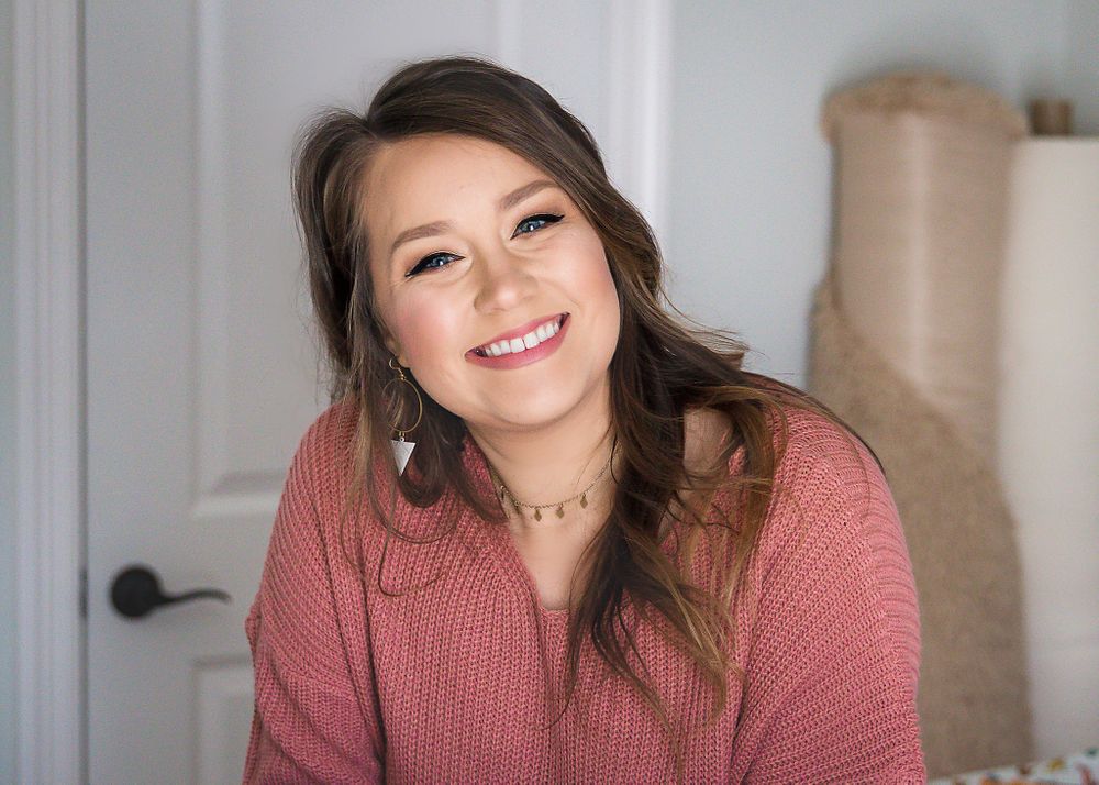 Portrait of woman in pink sweater smiling warmly against light interior wall.