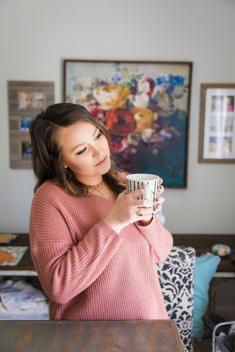 Person in pink sweater holding coffee mug near wall with vibrant floral artwork.