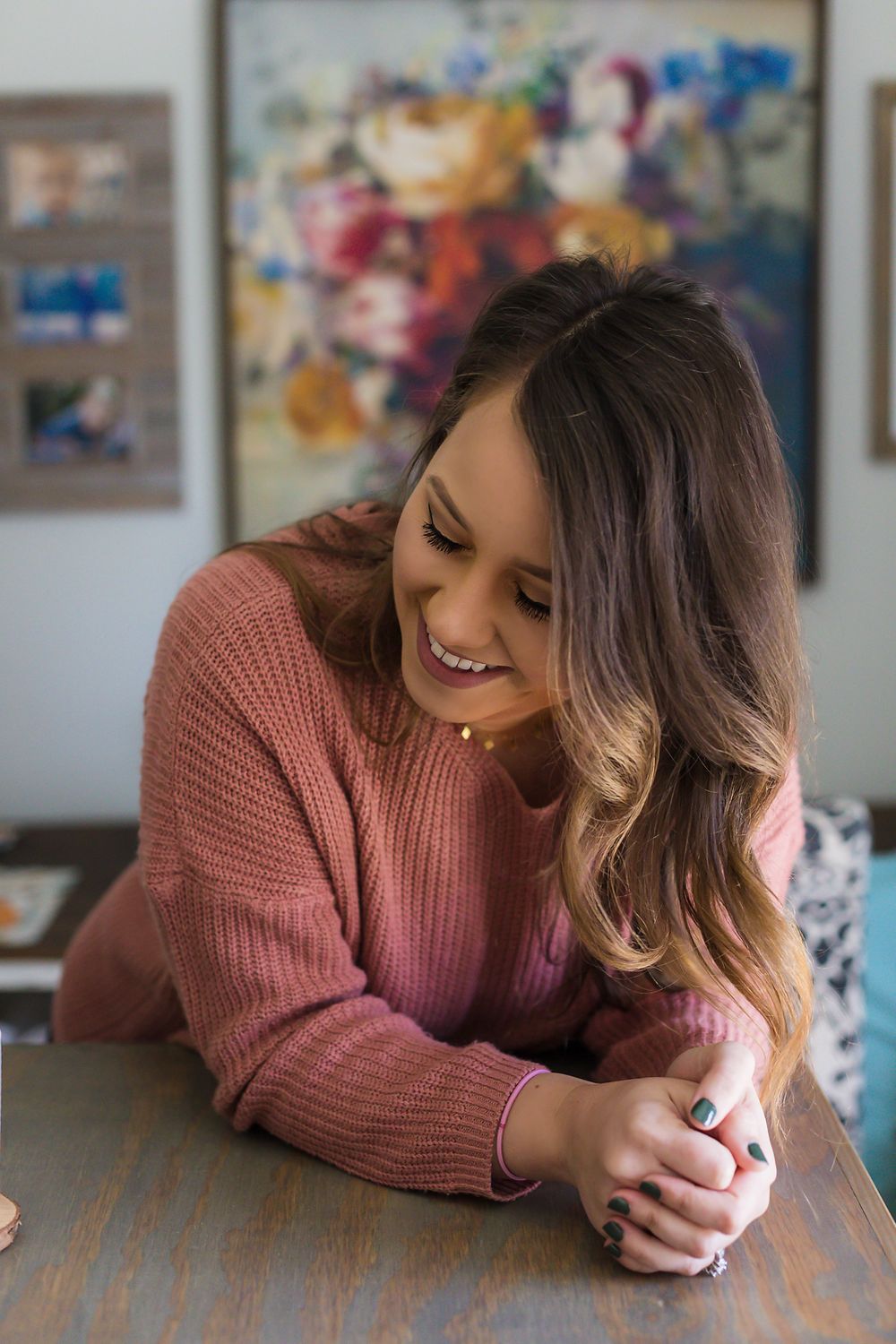 Candid moment of someone in pink sweater leaning on wooden table with vibrant art wall decor.