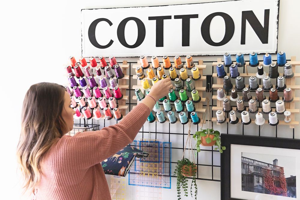 Person in pink sweater selecting thread from colorful cotton thread display wall.