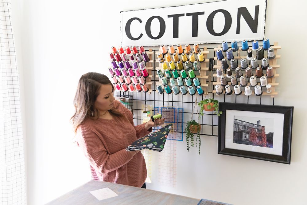 Person in salmon sweater organizing colorful thread spools on wall display under Cotton sign.