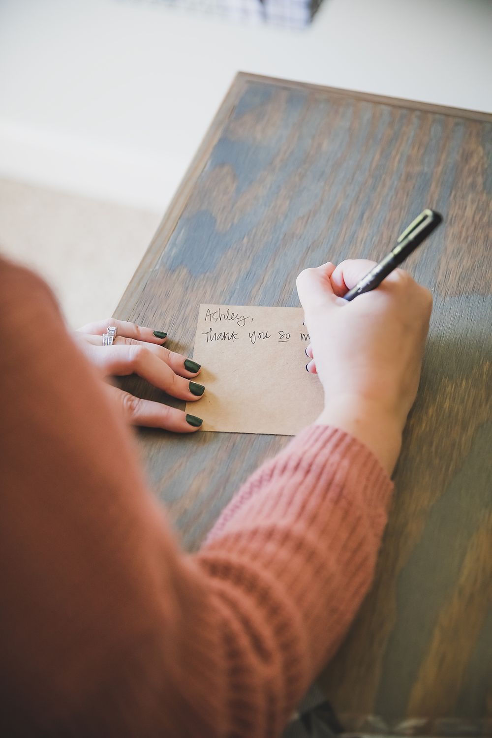 Close-up of hands in pink sweater writing note on paper at wooden desk.