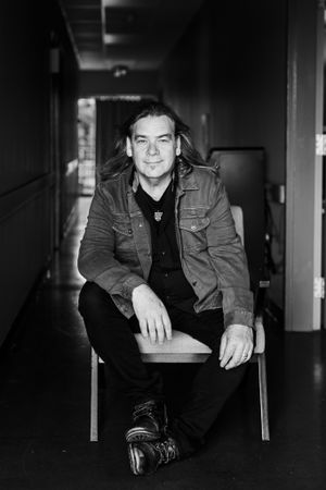 Alan Doyle, of Great Big Sea Fame, sits with the wind leaning forward in a chair.