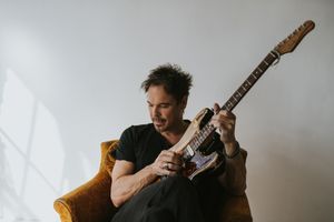 Ian Thornley of Big Wreck sits in a yellow armchair playing his guitar, glancing to the right of the frame.