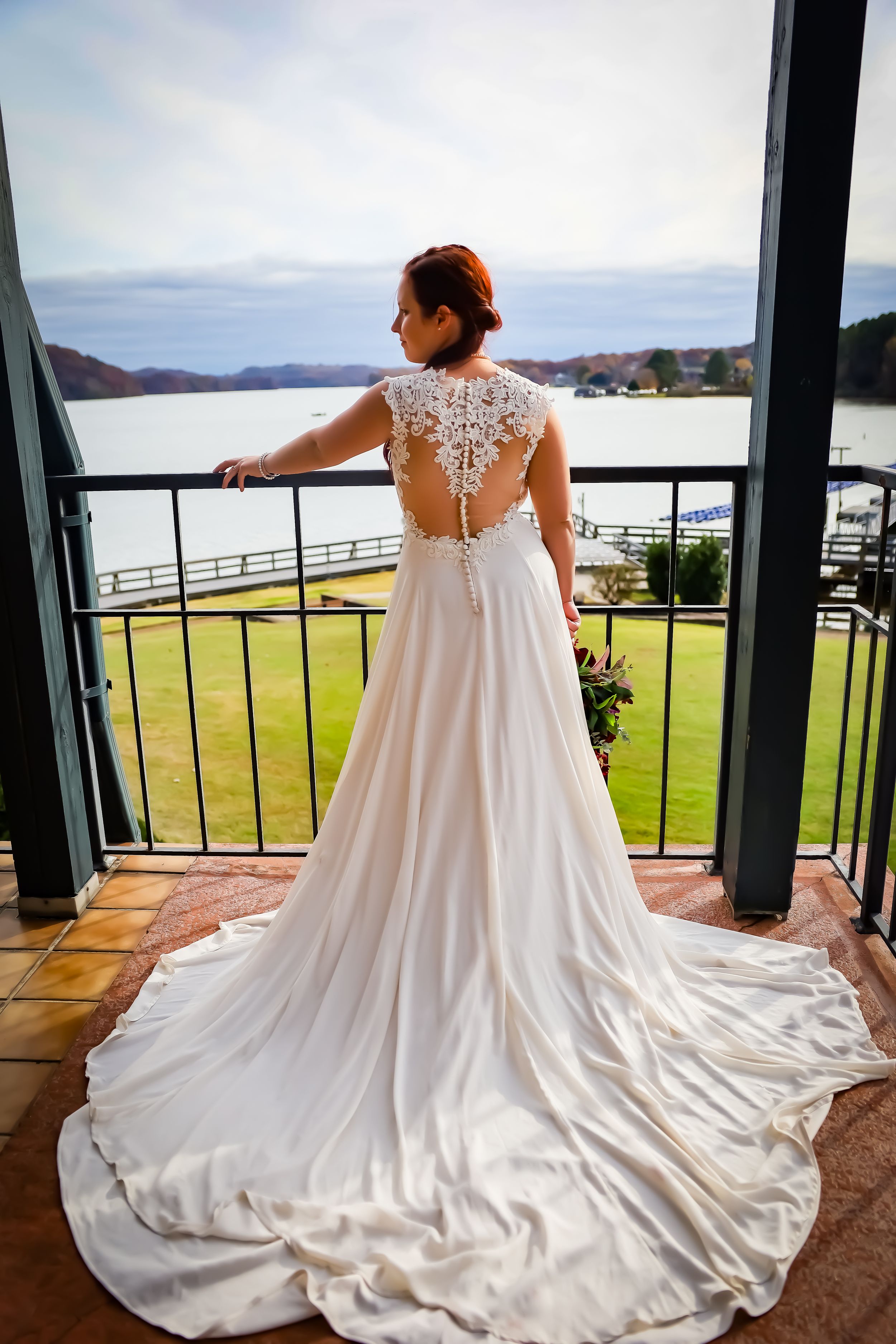 Wedding dress with intricate lace back and long train photographed on oceanfront terrace.