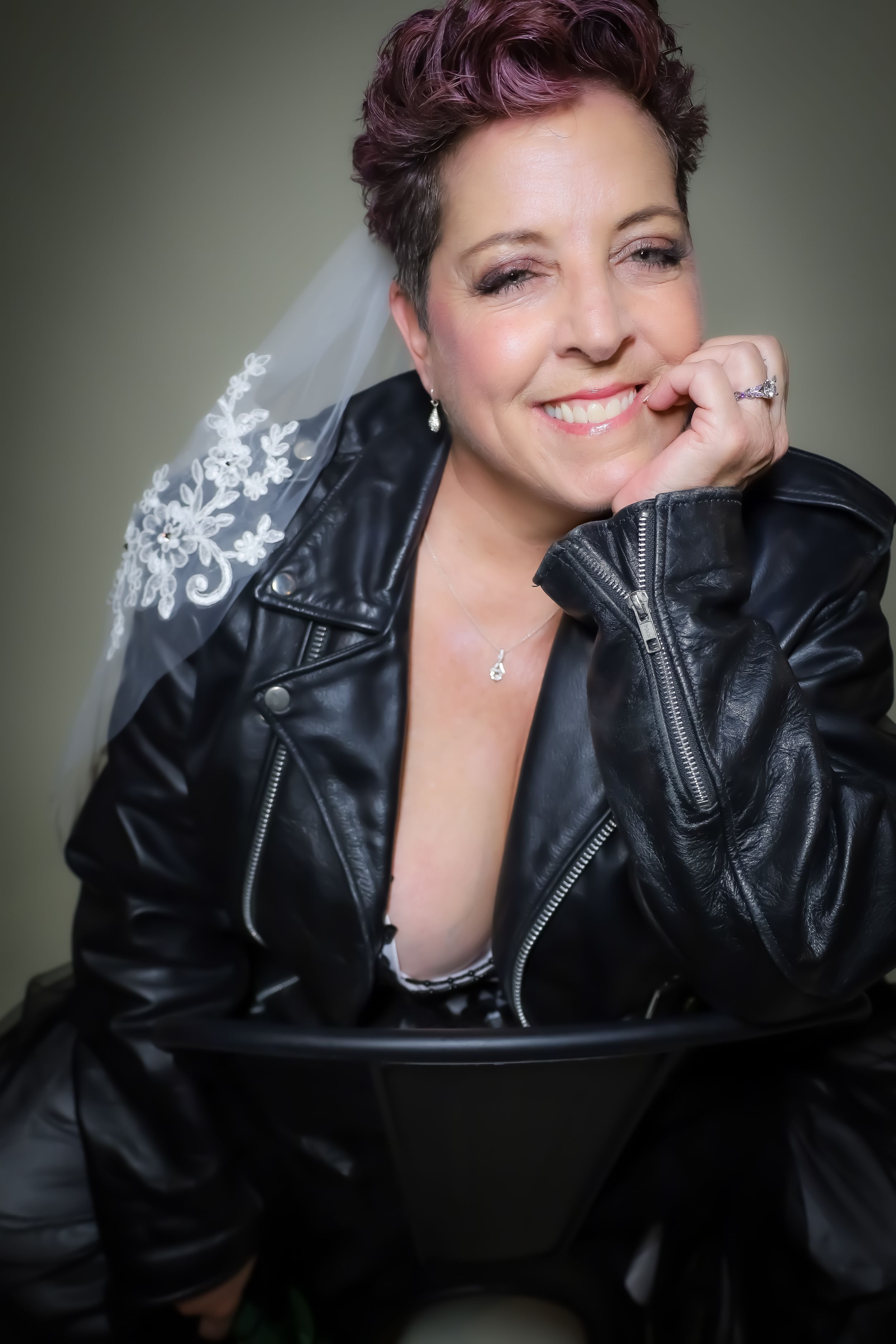 Portrait in black leather jacket with sparkly bridal accessories against grey background.