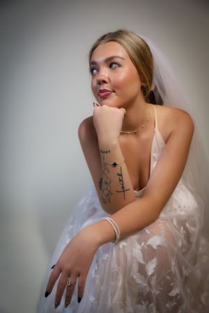 Bride in white lace dress shows delicate details and tattoo art in artistic bridal portrait series.