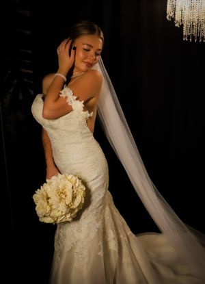 Dramatic bridal portrait with white roses against dark background showcases lace wedding dress details.