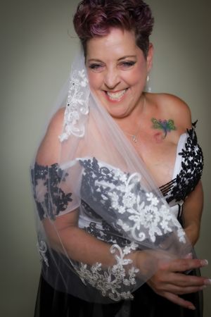 Bride wearing black and white dress with lace veil smiles during wedding portrait session.