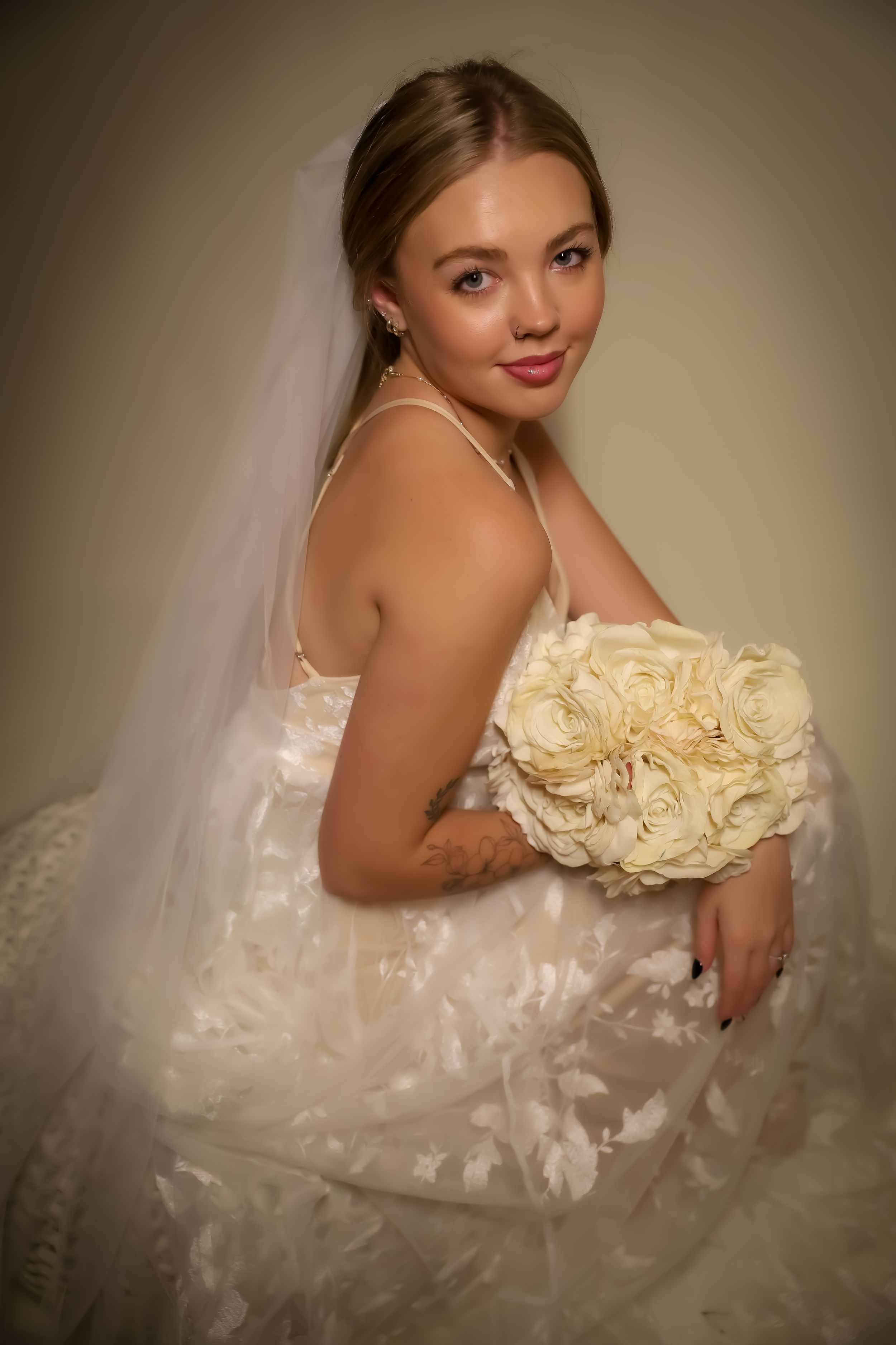 Bride in strapless gown poses with cream rose bouquet in romantic studio lighting.
