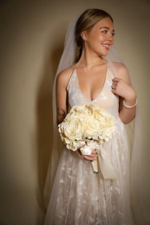 Elegant bride holding cream roses poses in flowing white gown with veil.