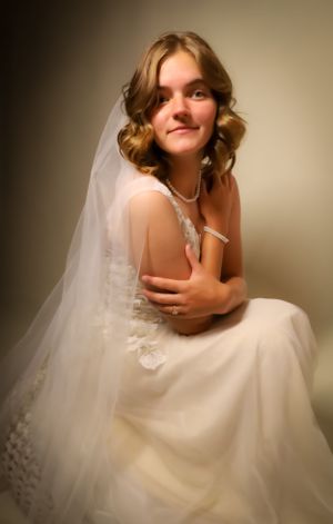 Dreamy bridal portrait shows bride sitting in voluminous white wedding gown.