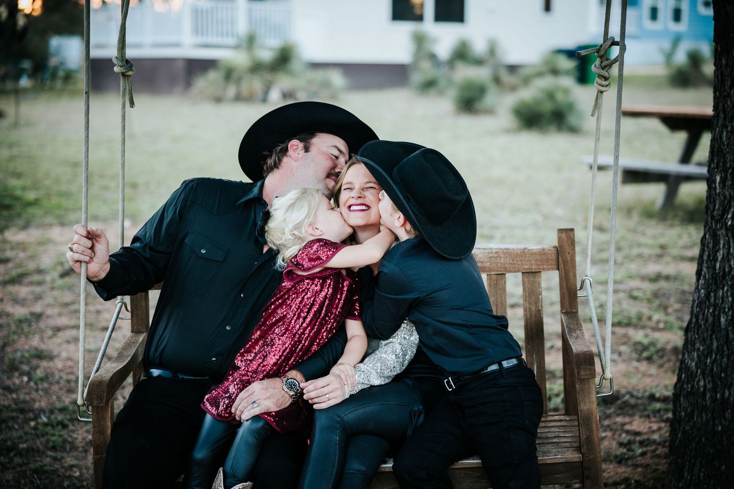 family sitting on bench swing parents kids children mom getting kissed