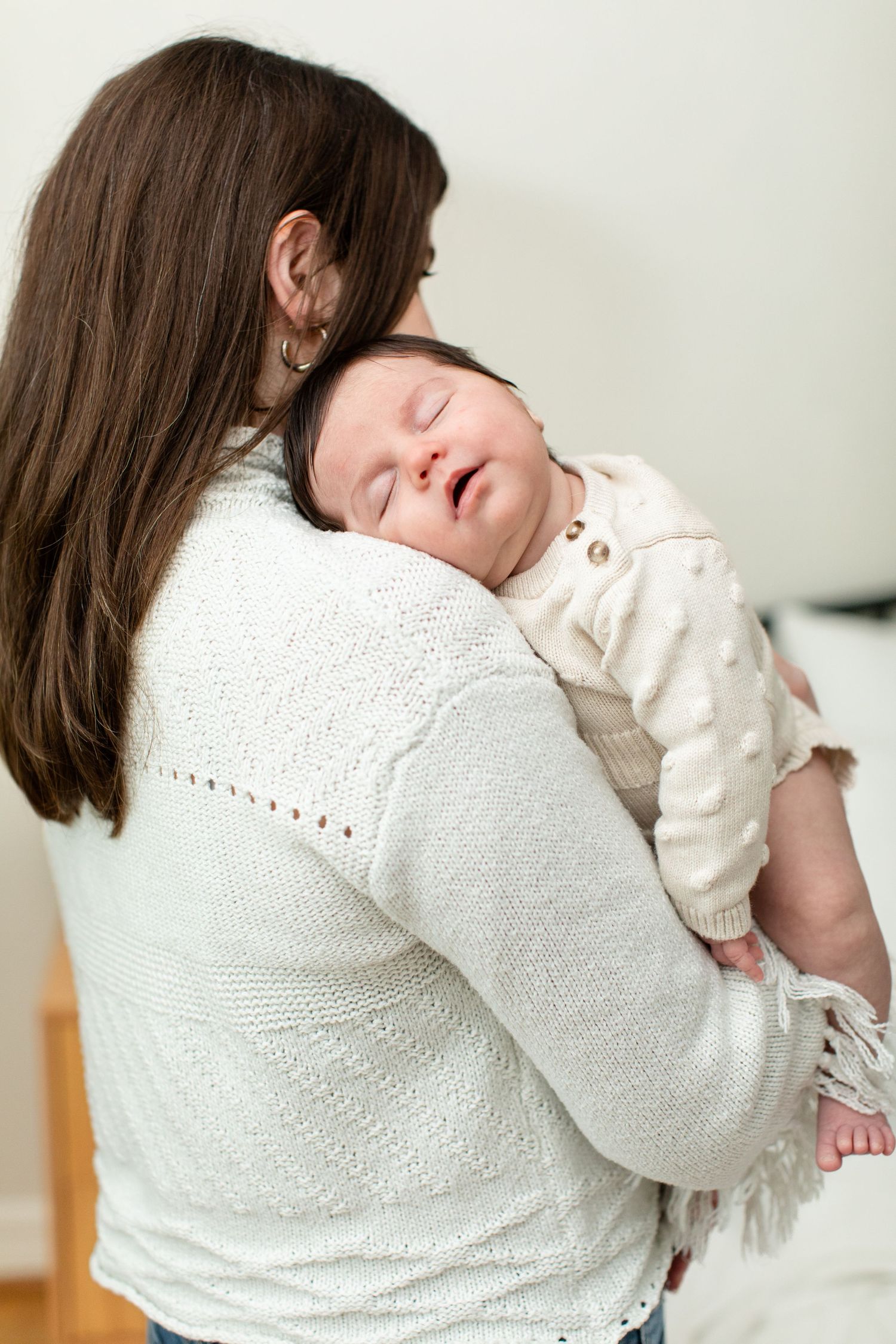 A sleeping newborn nestles against a caregiver's shoulder in a white sweater.