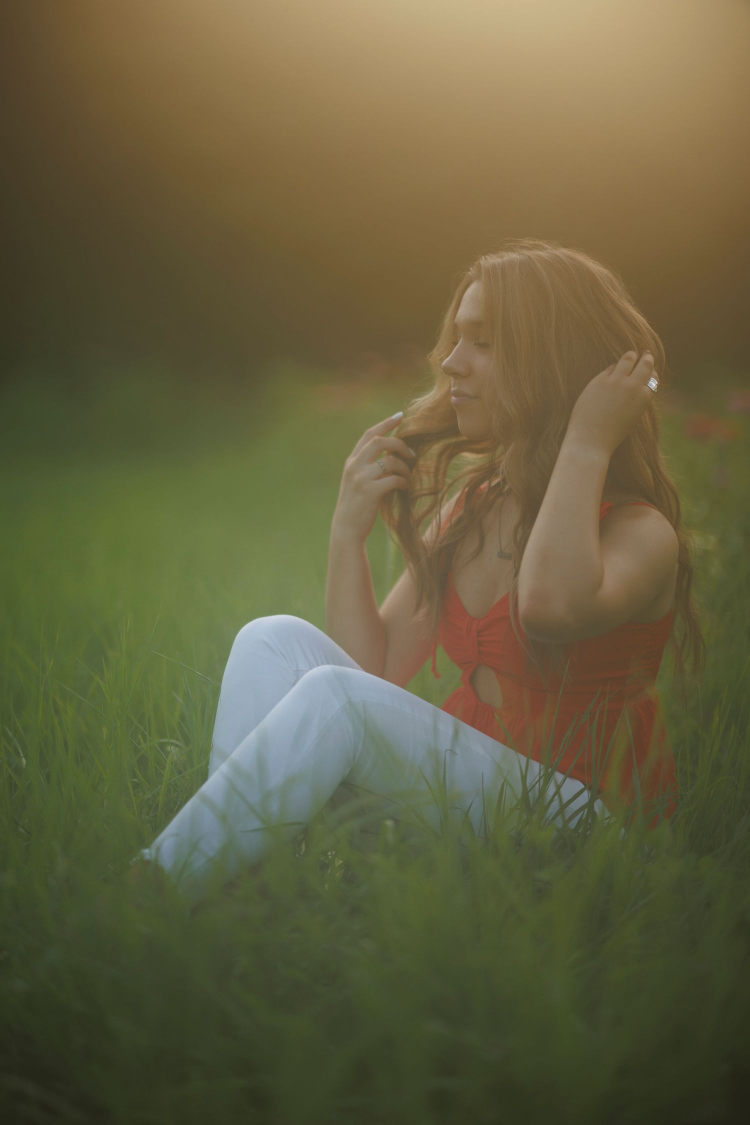 Dreamy golden hour portrait of someone sitting in tall grass wearing a red top.