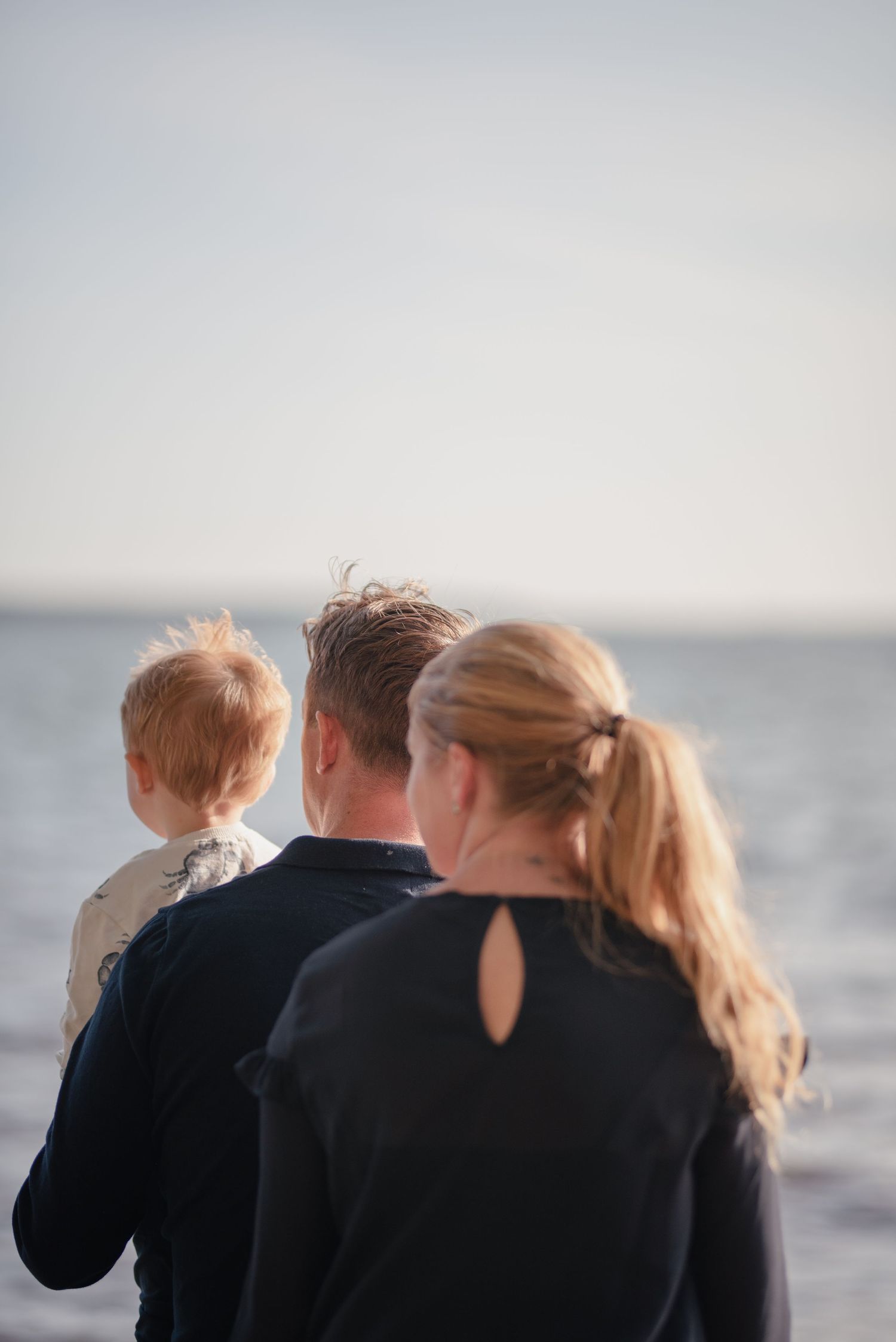 Group in dark clothing gazing out at the ocean from a rocky shoreline.