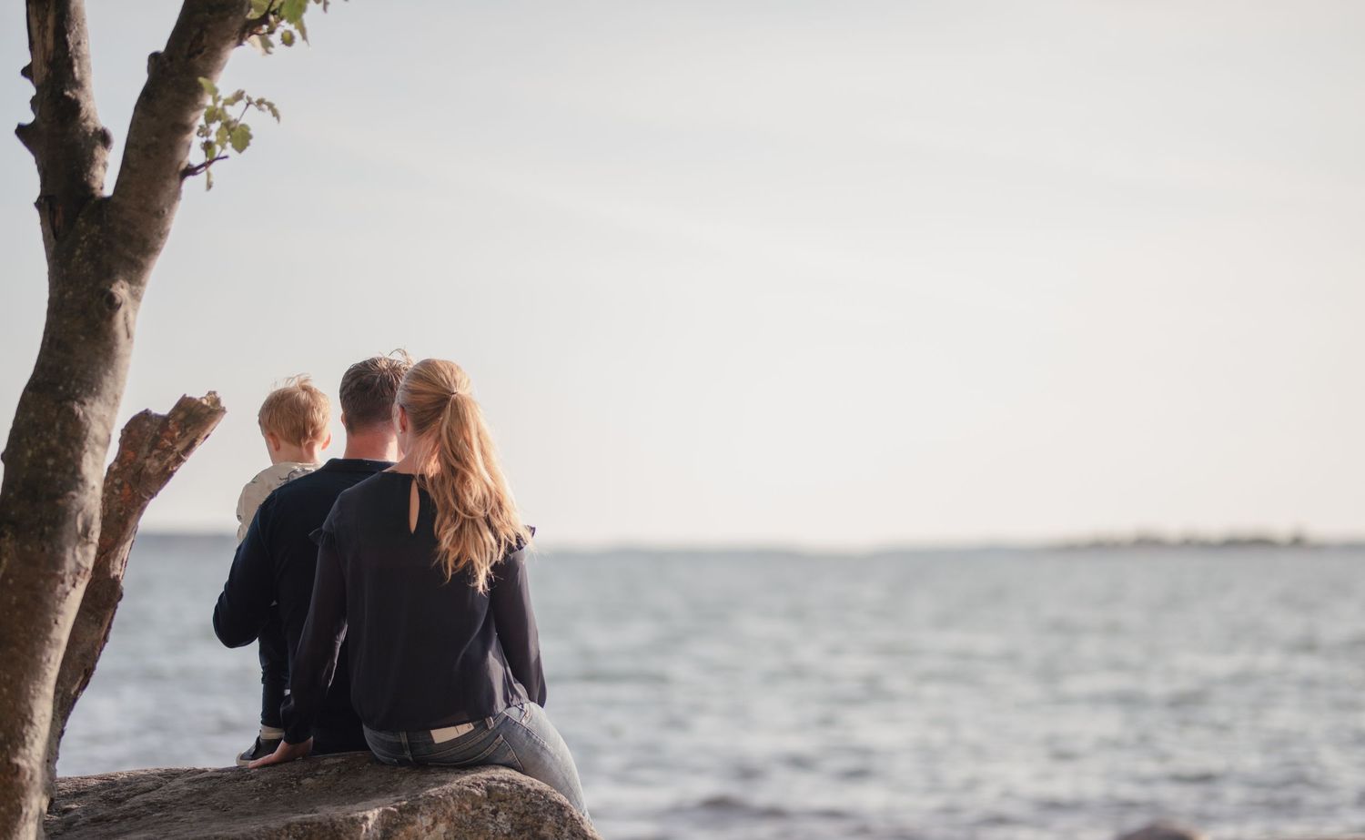 Figures sitting on a large rock by the ocean at sunset enjoying the peaceful view.