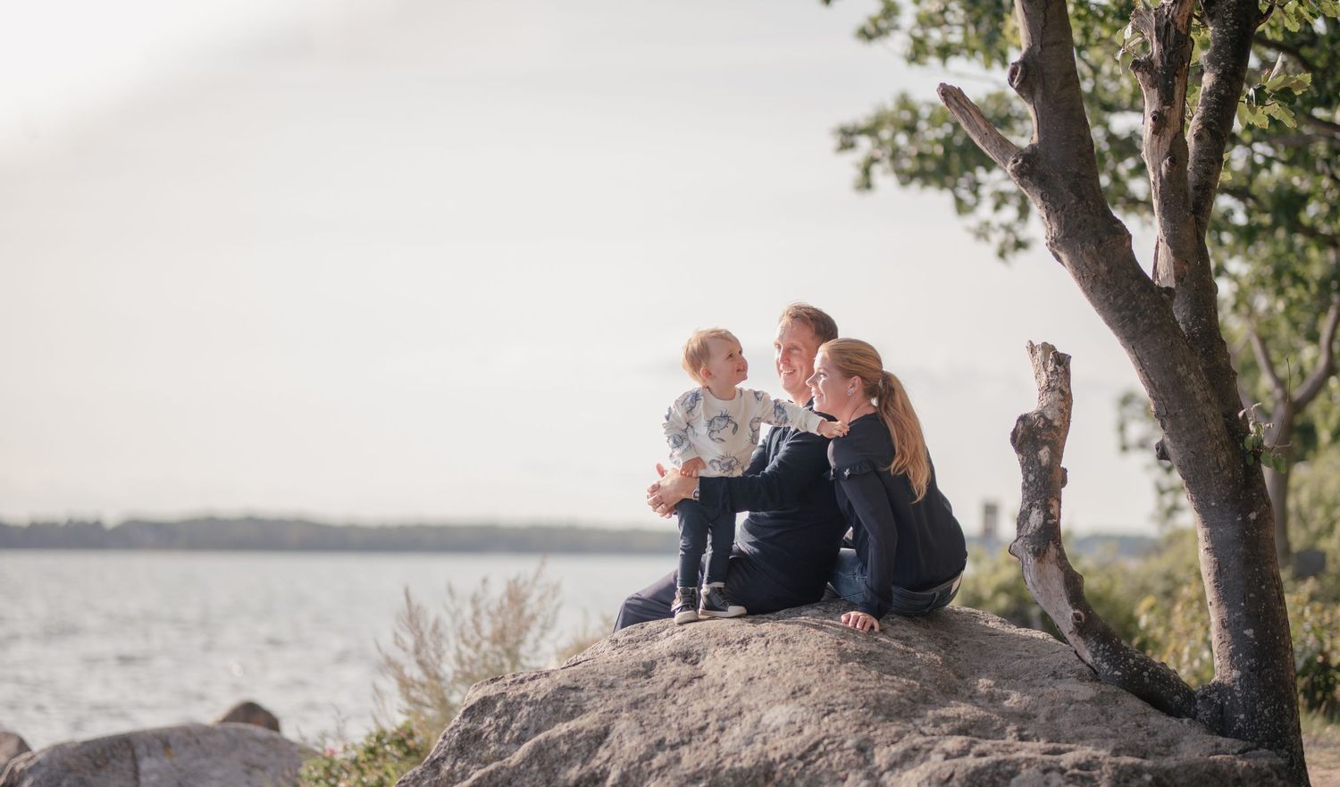 Family enjoying a coastal view while sitting together on a large boulder.