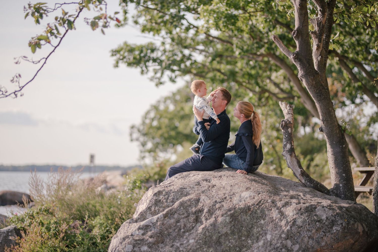 Two people sitting on a large coastal rock enjoying the waterfront view.