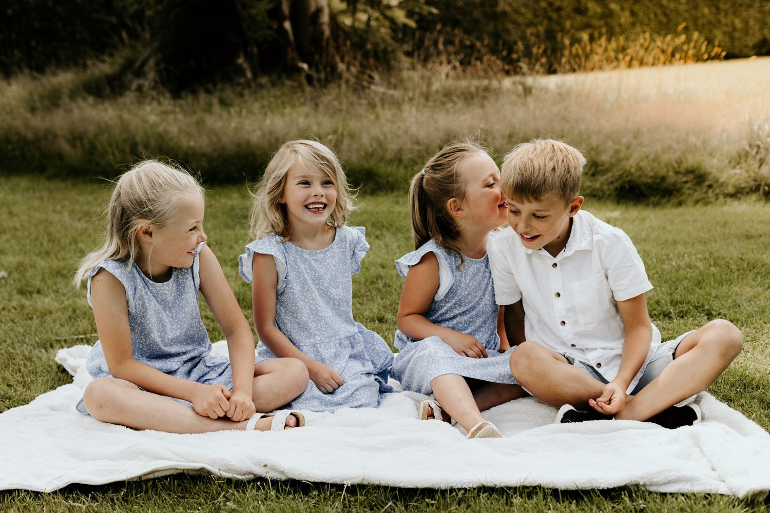 A group sitting on a white blanket enjoying a sunny summer day outdoors.