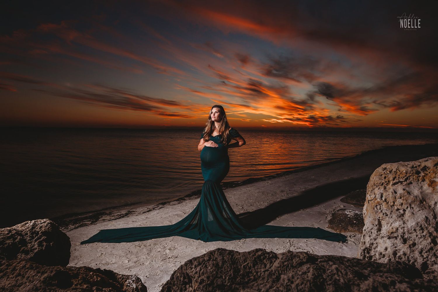 Silhouetted maternity portrait against vibrant sunset sky over ocean.