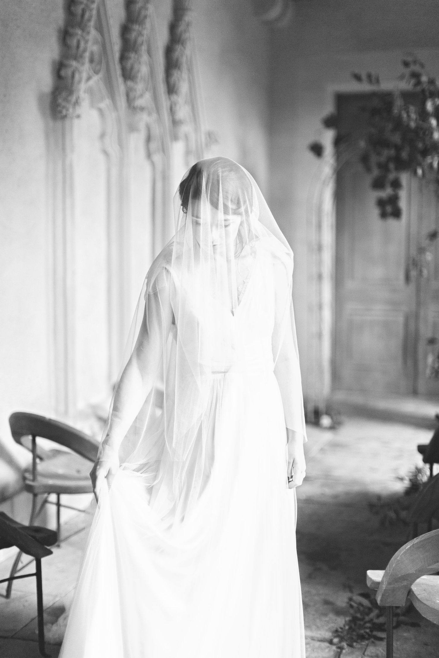 Black and white elegant wedding photo showing a figure in a white flowing dress and long veil standing indoors euridge manor