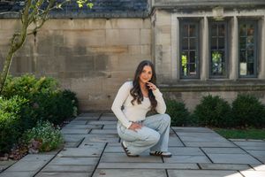 Young woman crouching on stone patio beside historic stone building exterior.