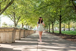 A woman in a floral skirt walks along a tree-lined park pathway.